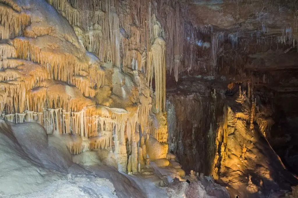 This image showcases the stunning natural beauty of a cavern with various formations. You can see stalactites, stalagmites, and other limestone formations in rich, warm tones, illuminated by strategically placed lighting. This subterranean landscape, full of delicate and intricate geological features, is an intriguing sight, ideal for exploring and appreciating the wonders of natural underground formations.