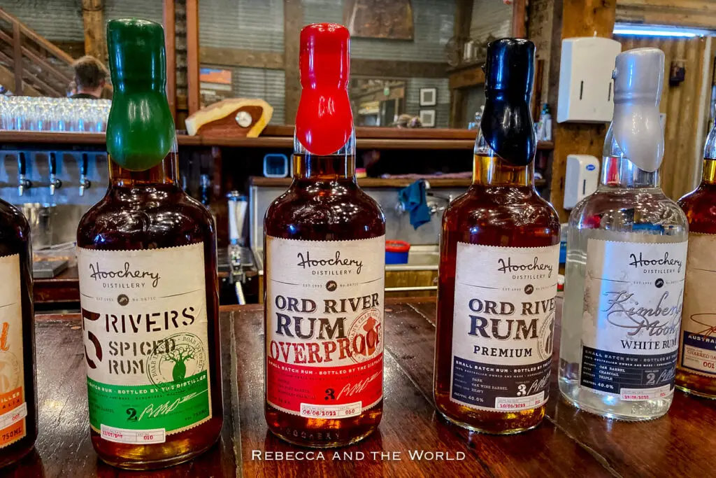 A row of bottles of rum from Hoochery Distillery displayed on a wooden bar. The labels include "Ord River Rum," "Kimberley Moon," and "5 Rivers Spiced Rum." A rum tasting at Hoochery Distillery is one of the best things to do in Kununurra.