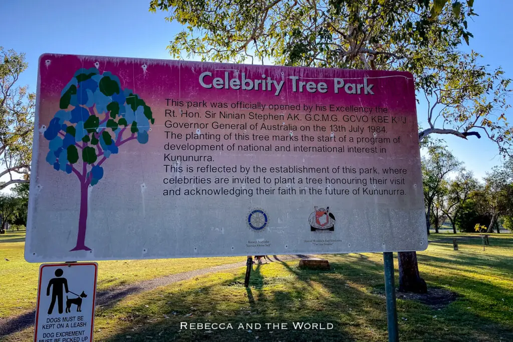 A large informational sign for Celebrity Tree Park, detailing its history and purpose. It is set in a grassy park area with trees and a smaller sign about dog regulations below it. Celebrity Tree Park is one of the more quirky things to do in Kununurra.