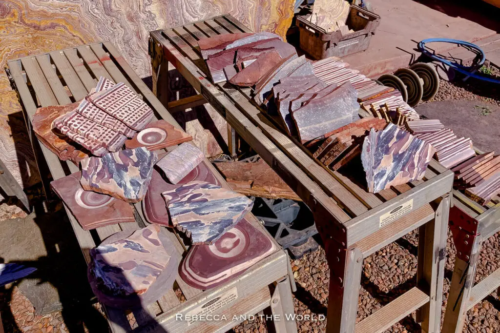 A display of various polished stones and slabs of colourful rock with intricate patterns. The stones are arranged on wooden tables under bright sunlight. These are samples of the patterned rocks found around Kununurra, which are repurposed into souvenirs and homewares.