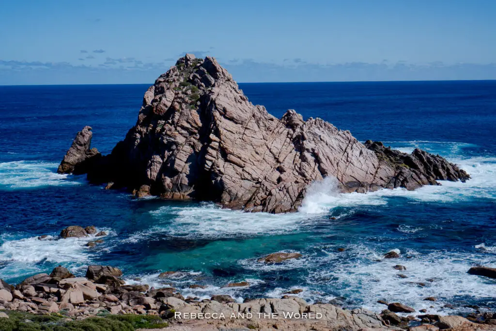 A striking rock formation known as Sugarloaf Rock stands prominently in the Indian Ocean off the coast of Western Australia. The jagged, granite rock juts out of the deep blue water, creating a dramatic seascape that is popular among tourists exploring the Margaret River region.