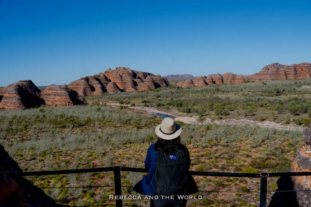 A woman - the author of this article - in a tan-coloured hat standing at an overlook, gazing out at the expansive Bungle Bungle Ranges in Purnululu National Park. The scene shows the vast, layered rock formations stretching into the distance.