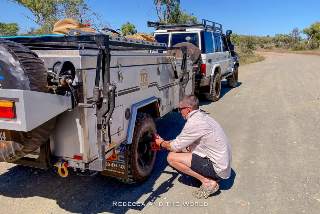 A man - the author's husband - adjusting tyre pressure on a trailer attached to a four-wheel-drive vehicle on a dusty road in Purnululu National Park. A tyre pressure kit is a must when travelling through the Bungle Bungles.