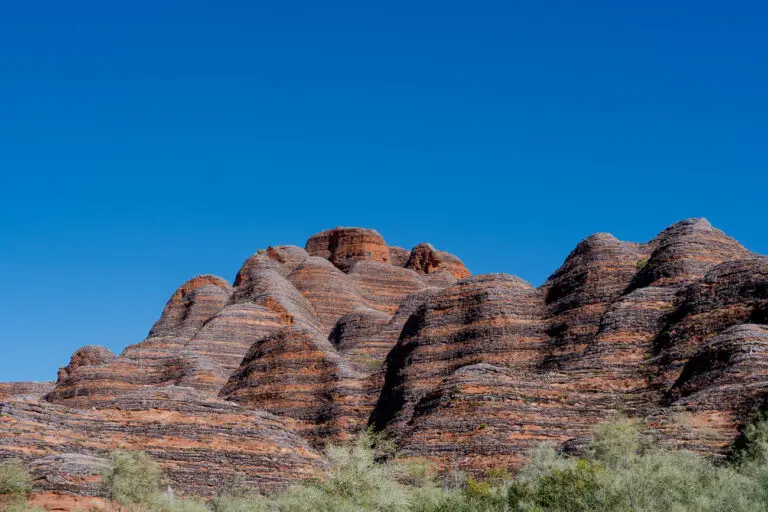 A close-up view of the iconic beehive-shaped domes of the Bungle Bungle Ranges in Purnululu National Park. The domes feature distinctive horizontal stripes of orange and black, under a bright blue sky, showcasing the park’s striking geological formations.