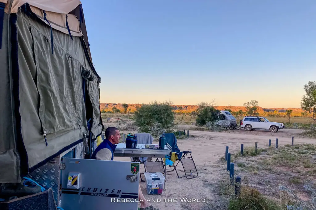 A campsite set up in the rugged Kimberley outback, with a man sitting outside a large tent attached to a 4x4 vehicle. The campsite is at the Mimbi Caves Campground.