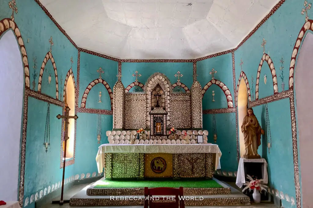 The ornate interior of the Sacred Heart Church, known for its unique design, is decorated with mother-of-pearl shell and other local materials. The turquoise walls and detailed altarpiece are adorned with shell motifs and religious symbols.