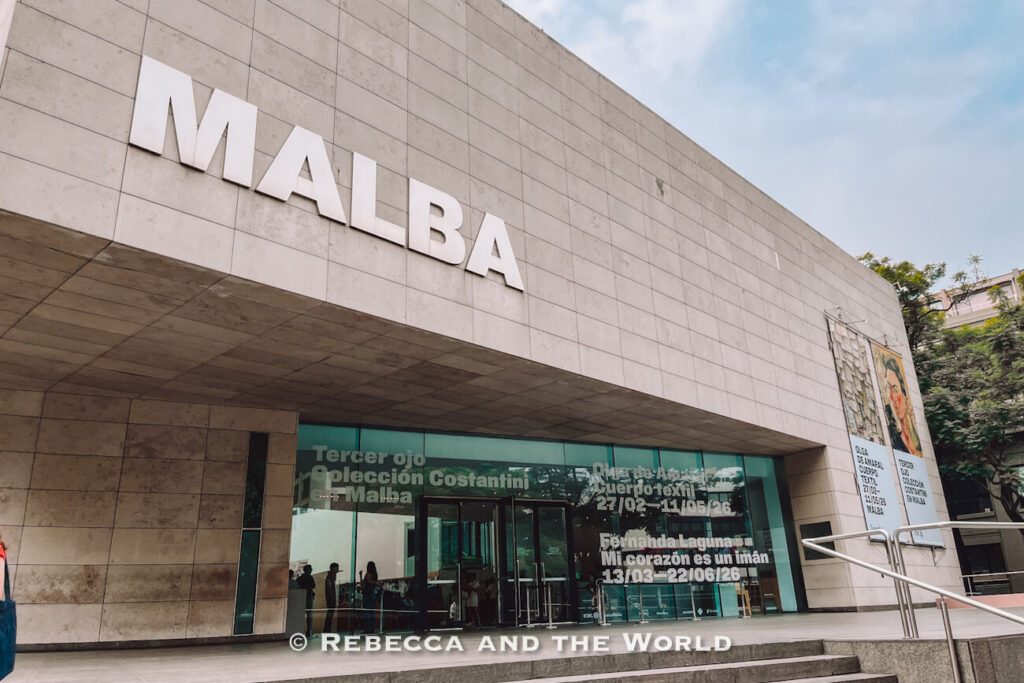 Exterior of the MALBA museum building with a modern stone facade and large glass entrance. The sign “MALBA” is prominently displayed above the entrance. Visitors can be seen inside through the glass doors. Visiting museums like this is often included in a 3 days in Buenos Aires itinerary.