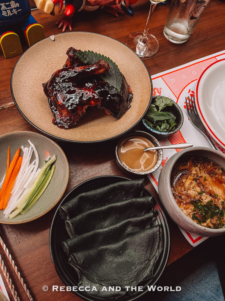 A table filled with plated dishes, including glazed meat, sauces, vegetables, and folded wraps. Glassware and utensils are arranged around the setting. Trying a variety of foods like this is a highlight of any Buenos Aires itinerary.