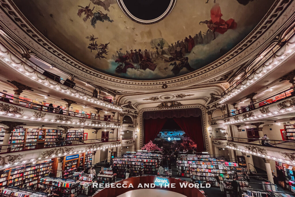 Interior of a grand bookstore set inside a former theater, with balconies lined with bookshelves and a stage at the far end. People browse and walk through the space. Visiting El Ateneo Grand Splendid bookshop is one of the most iconic things to do in Buenos Aires.
