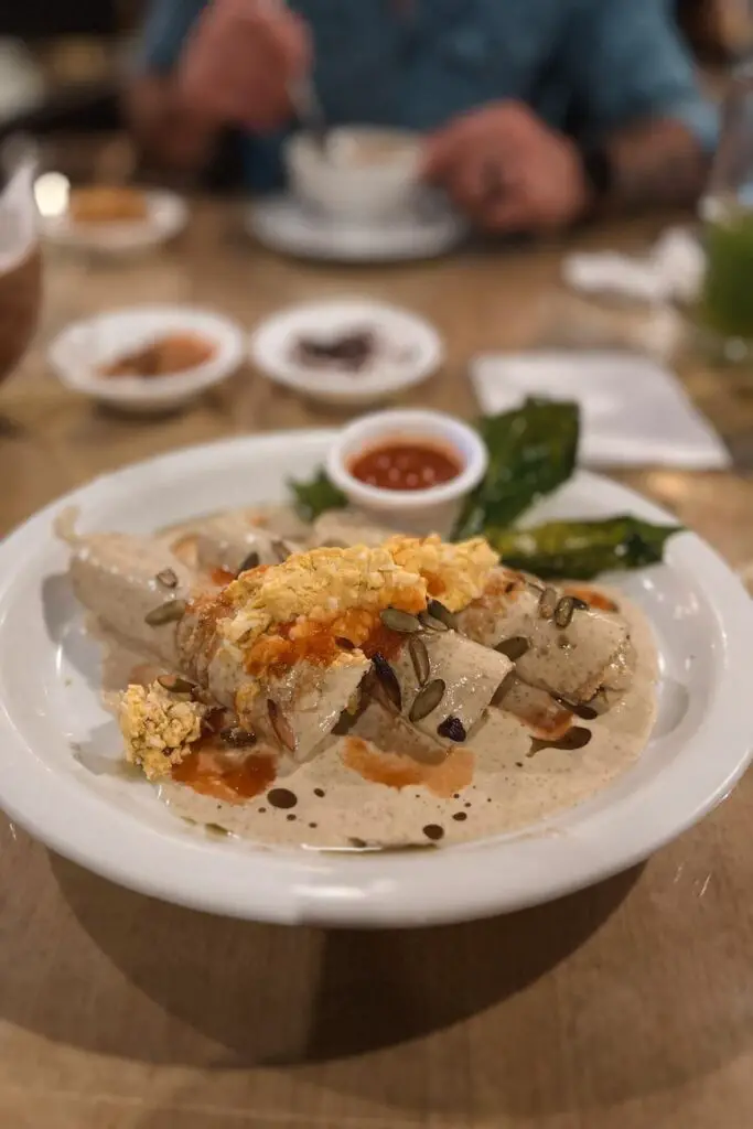Traditional Yucatecan dish called papadzules, topped with pumpkin seed sauce, eggs, and tomato salsa—essential for any food-focused Merida itinerary.