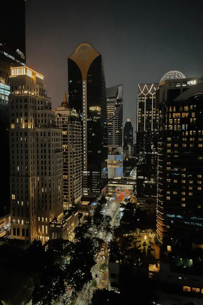 Bangkok’s cityscape lit up at night, showcasing tall office buildings, glowing windows, and bustling streets below.