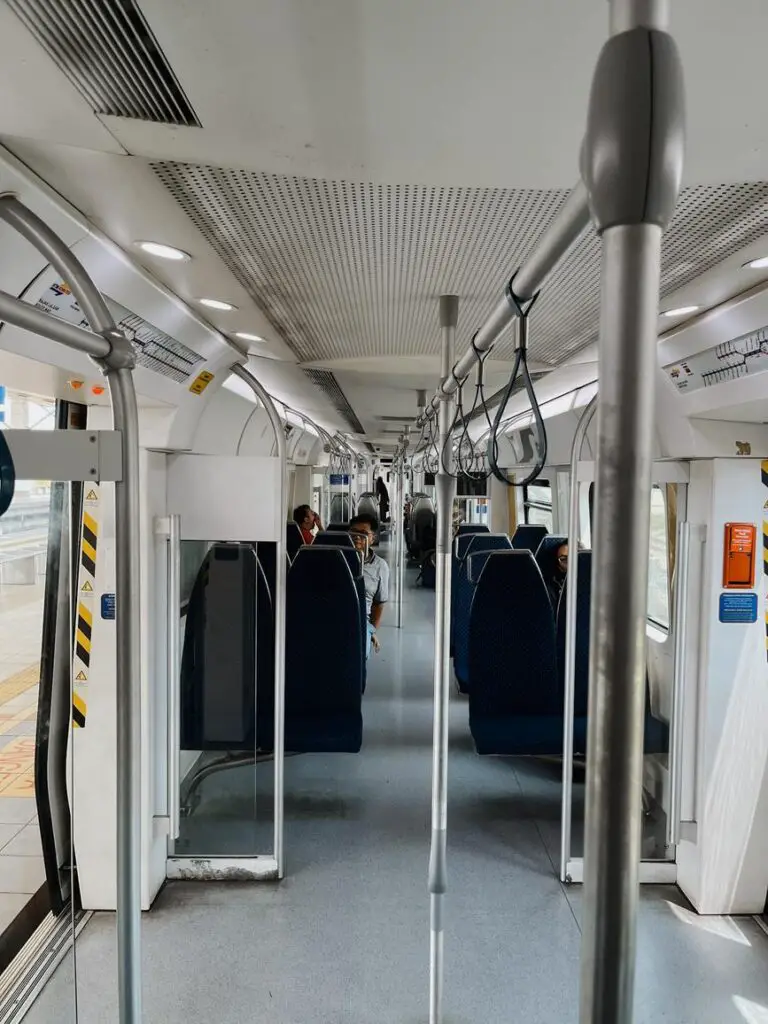 Interior of a modern commuter train travelling between Butterworth and Padang Besar in Malaysia with rows of blue seats, handrails, and passengers seated quietly during transit.