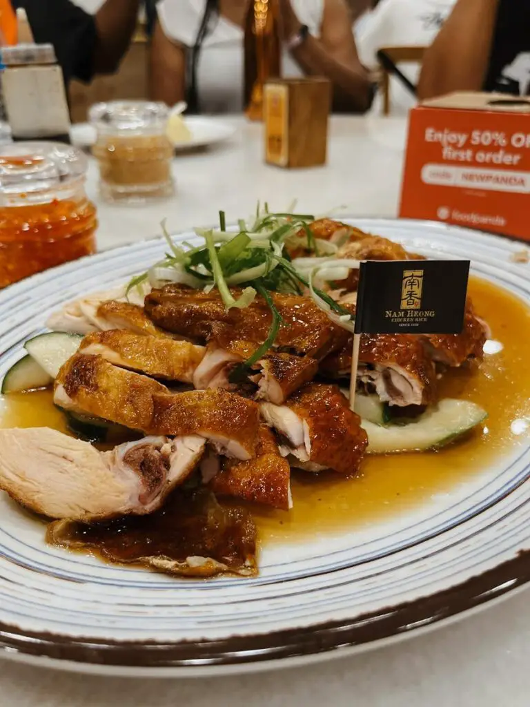 Plate of glistening roasted Hainanese chicken slices garnished with julienned cucumber and green onions, served in a light soy-based sauce during a food tour in Kuala Lumpur.