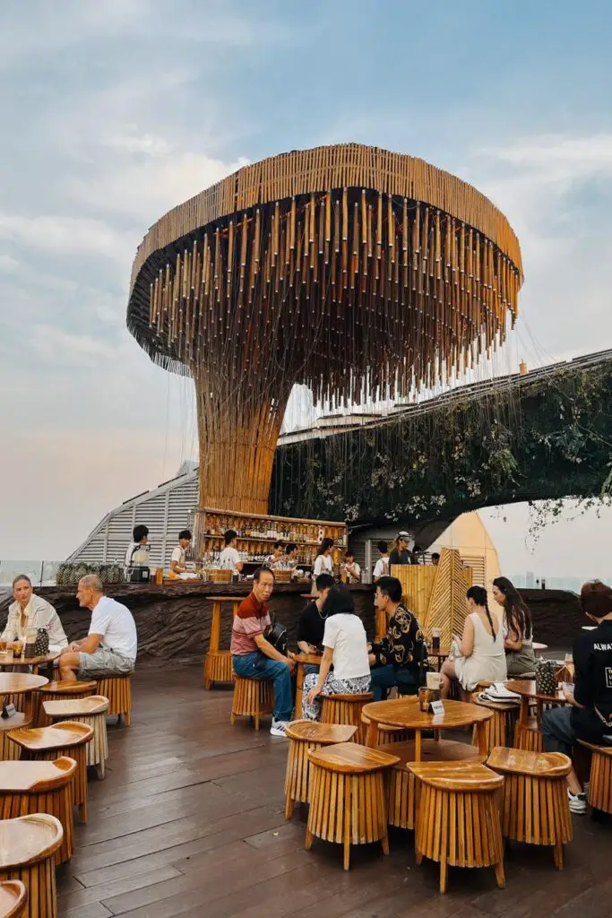 People seated at wooden tables under a large circular bamboo structure at the stylish Octave rooftop bar during sunset.