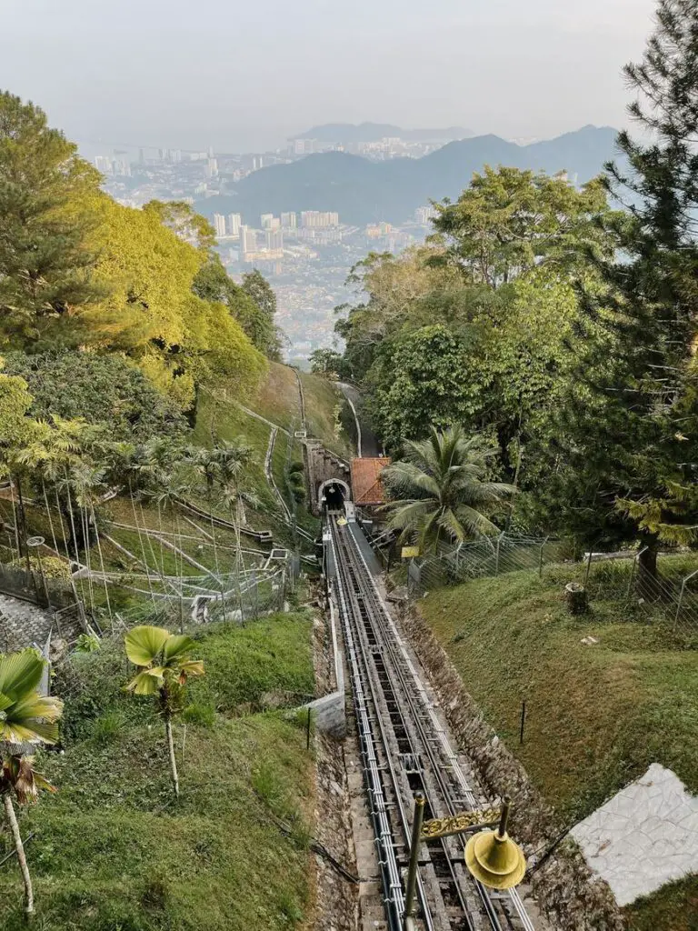 View from the top of Penang Hill showing the funicular railway tracks descending through lush greenery with George Town’s cityscape in the distance.