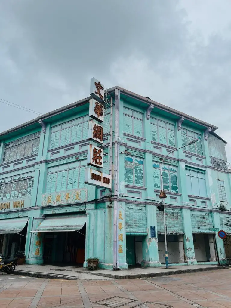 A turquoise-blue heritage building in Penang with worn paint and Chinese signage reading ‘Boon Wah,’ set beneath an overcast sky.