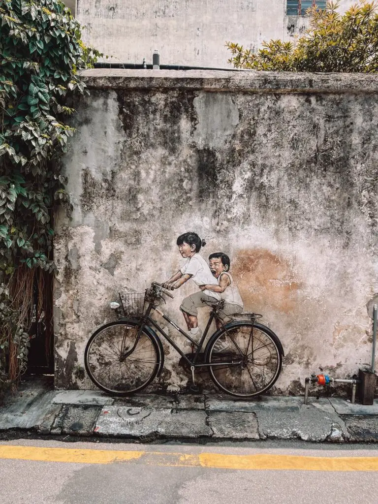 Famous Penang street art mural of two children riding a real bicycle affixed to a wall, with the painting integrating with the bike for a 3D effect.