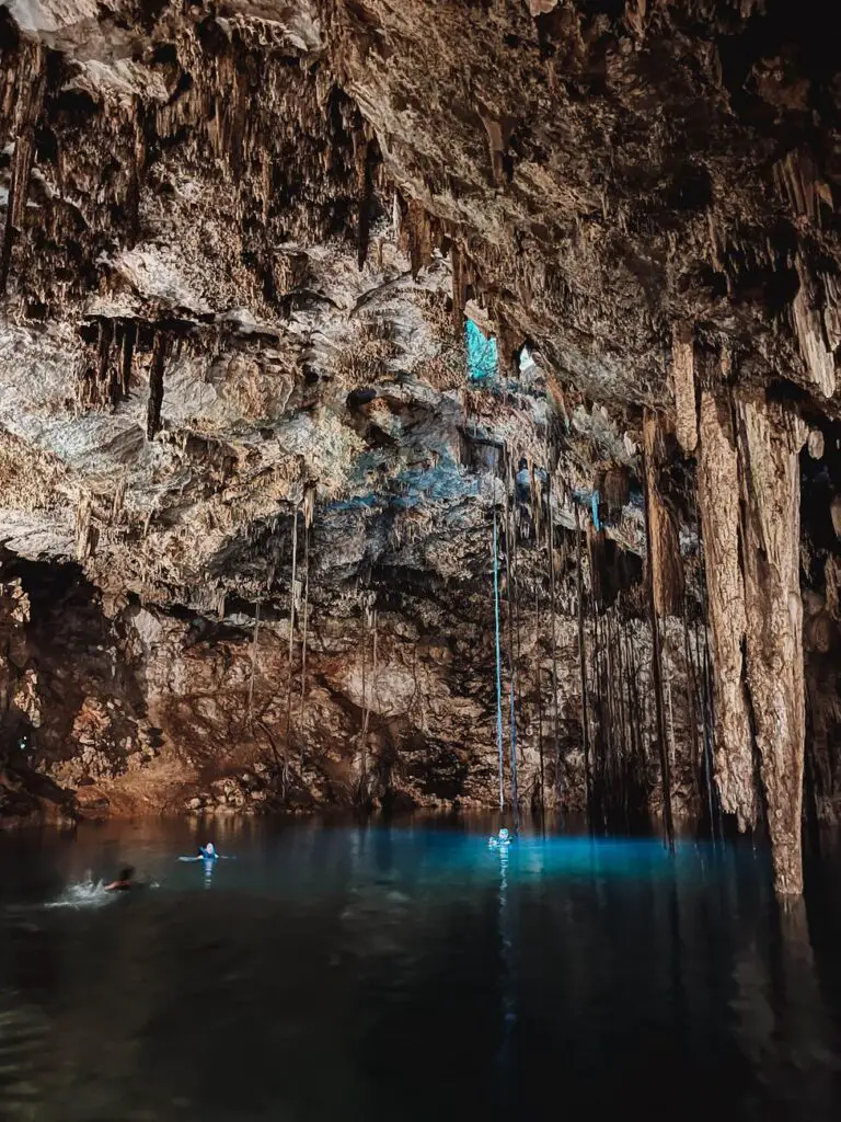 Swimmers float in the clear blue waters of Cenote Samula, a stunning underground cenote with dramatic stalactites in the Yucatan Peninsula.