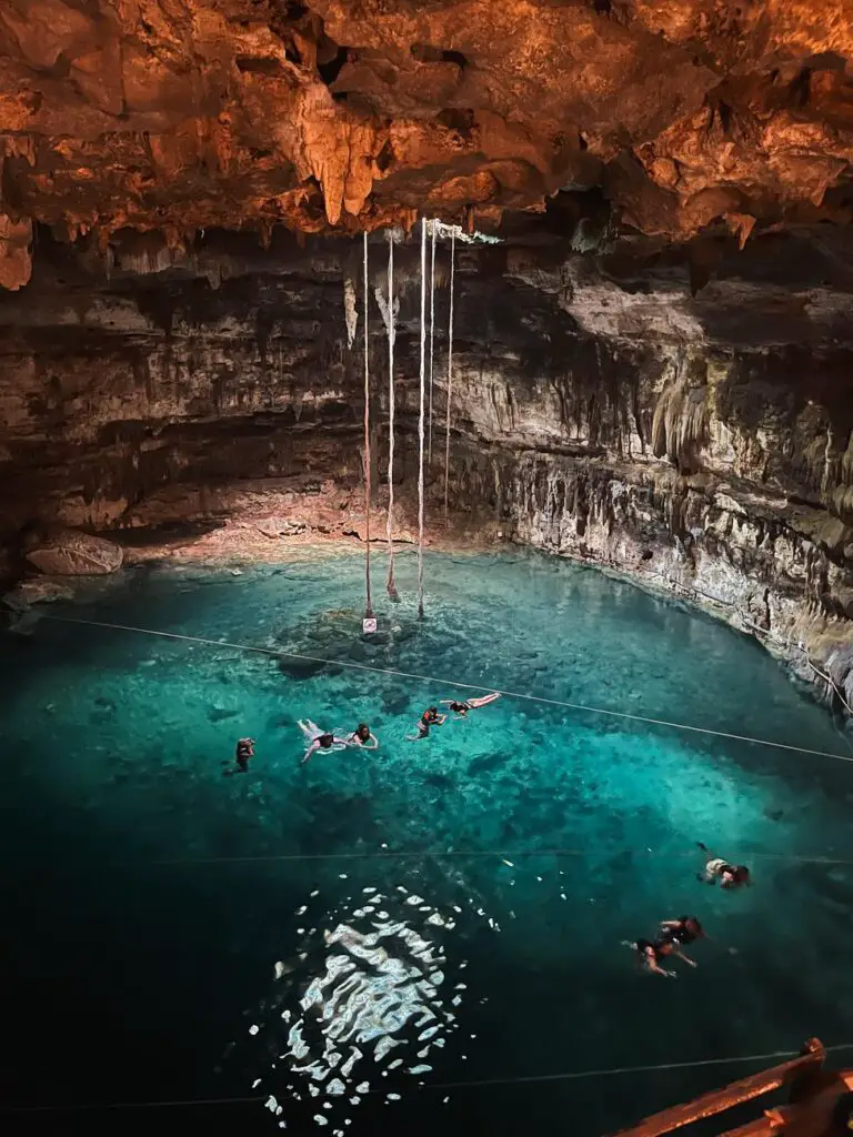 Travelers swimming inside Cenote X'keken, a striking underground cave cenote lit by shafts of light, popular on Yucatan itineraries.