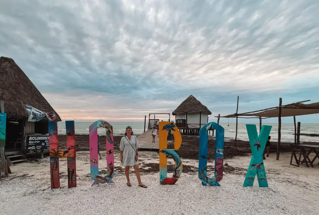 A woman - the author of this article - poses in front of the colorful Isla Holbox sign at sunset.