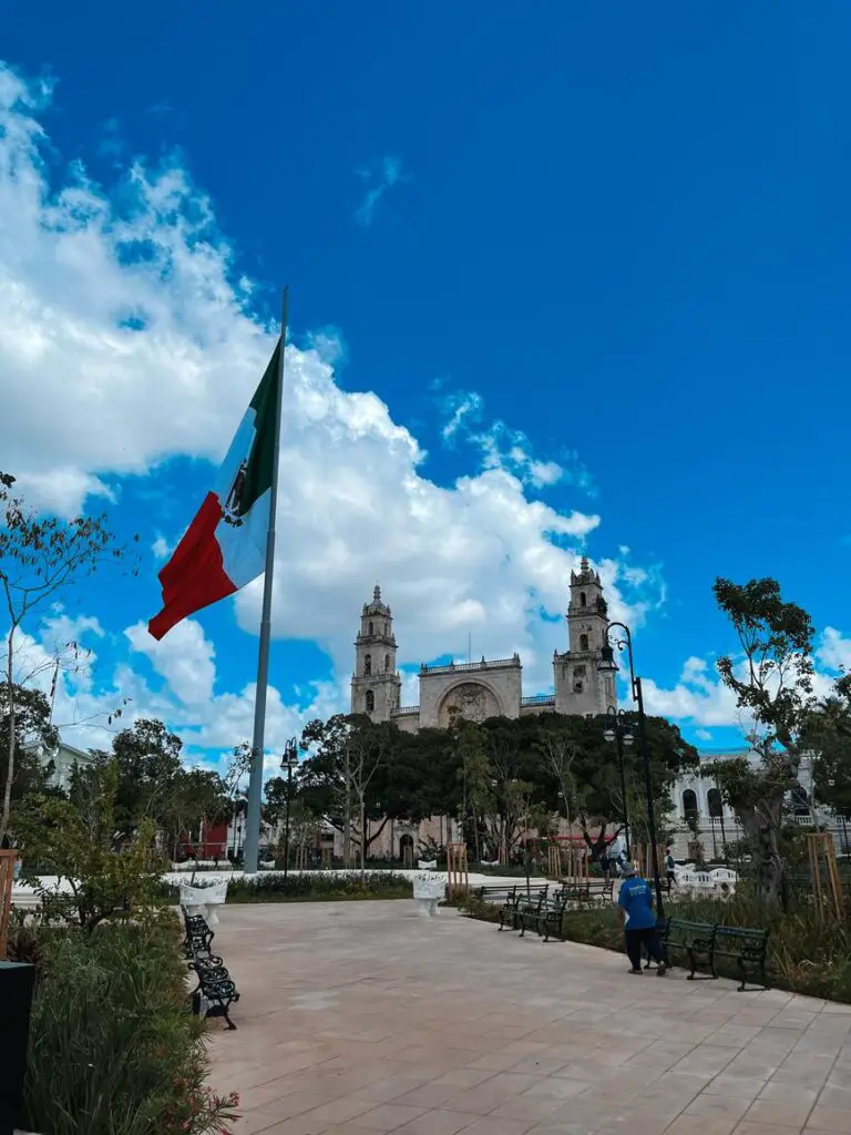 View of Plaza Grande in Merida with the Mexican flag and cathedral, a central landmark on a city walk.