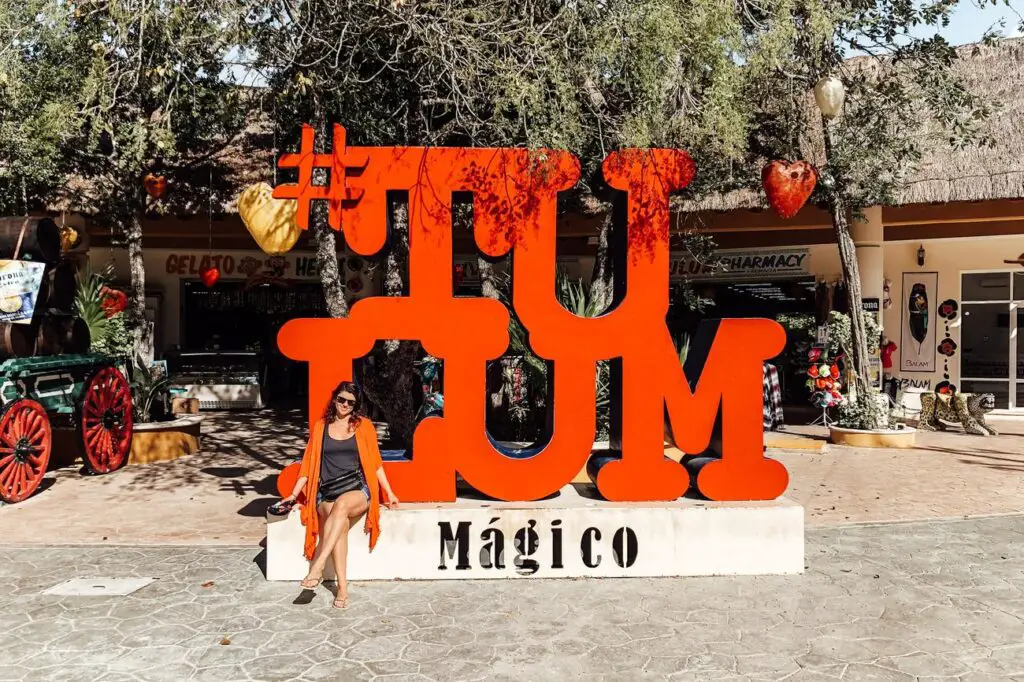 Woman - the author of this article - posing in front of the vibrant red Tulum sign.