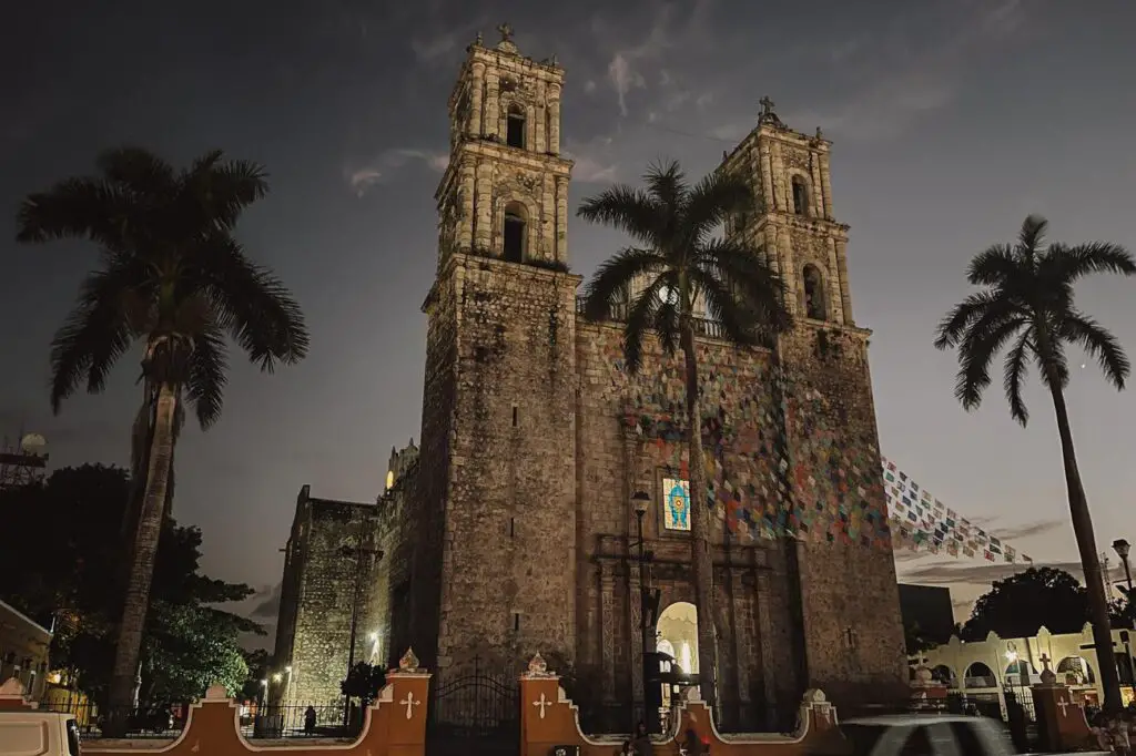 The illuminated façade of San Servacio Cathedral in Valladolid at dusk, with palm trees silhouetted in the foreground.