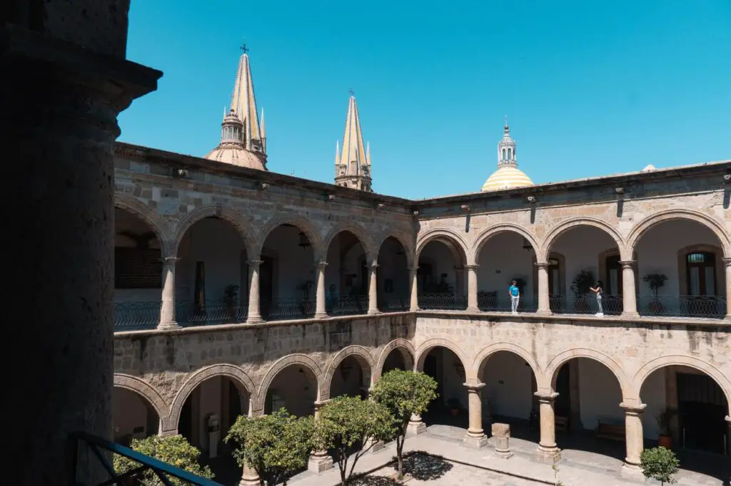 View of the arched courtyard inside Guadalajara’s Government Palace, with the city’s cathedral domes rising in the background—an essential stop for history and architecture lovers.