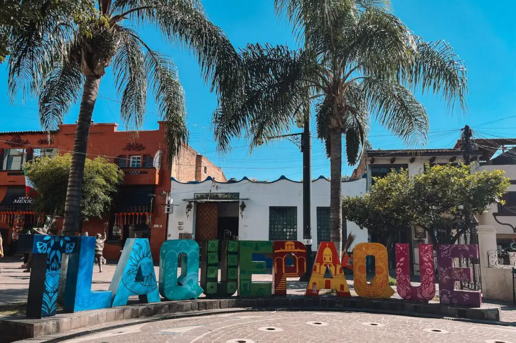 Brightly painted “TLAQUEPAQUE” sign in a leafy plaza, surrounded by palm trees and boutiques in this artistic suburb of Guadalajara.