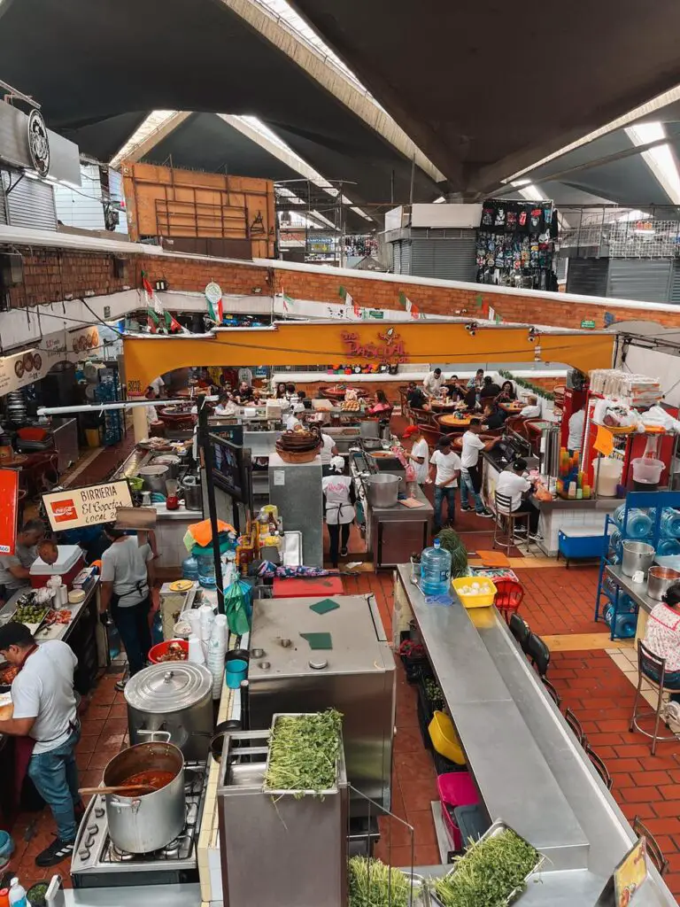 Bird’s eye view of a busy Guadalajara market filled with food vendors, locals dining at counters, and colorful signage—highlighting local life and cuisine. This is Guadalajara's Mercado Libertad, San Juan de Dios.