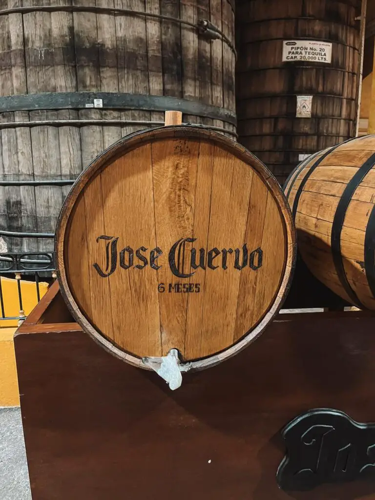 Close-up of a wooden tequila barrel marked "Jose Cuervo - 6 meses" inside the aging room of the Jose Cuervo distillery.
