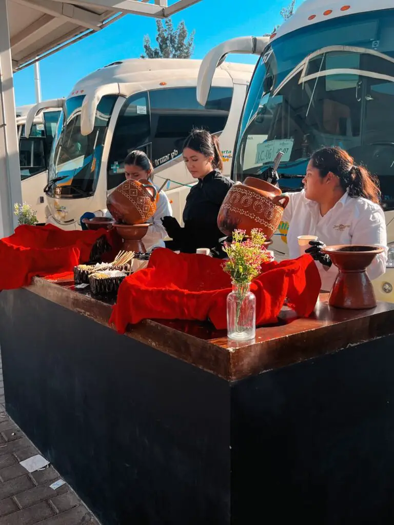 Women preparing snacks and coffee at a stand near buses outside the Jose Cuervo Express boarding area—offering local hospitality before the train ride.