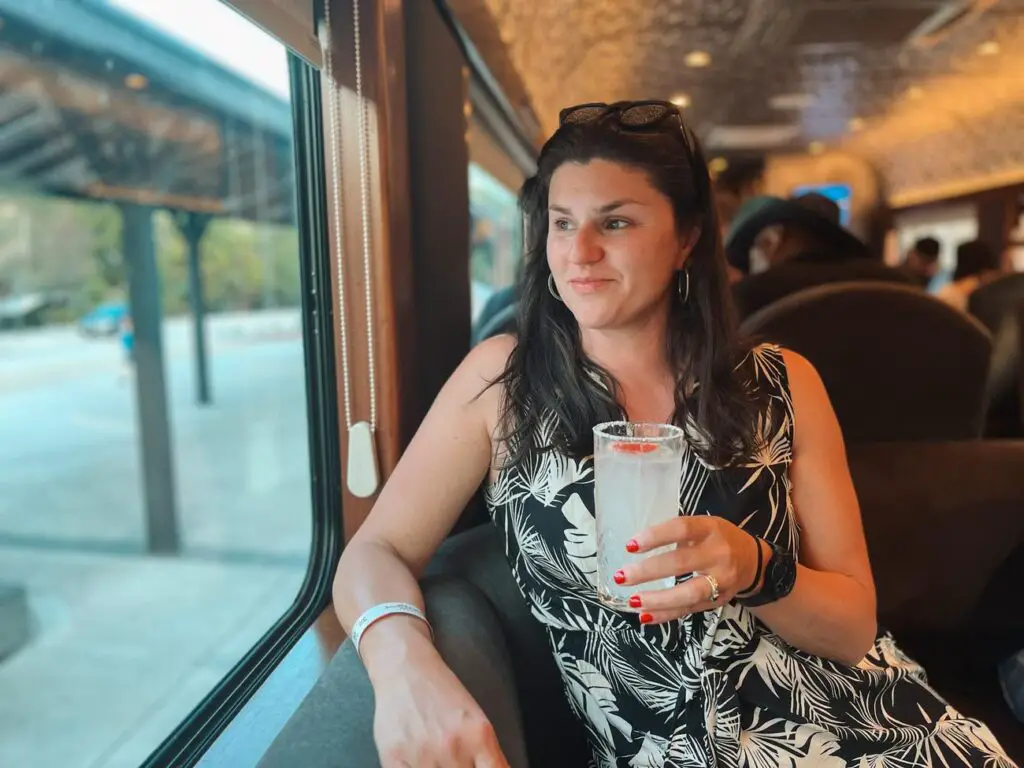 A woman - the author of this article - smiling and holding a tequila cocktail while seated by the window on the Jose Cuervo Express train.