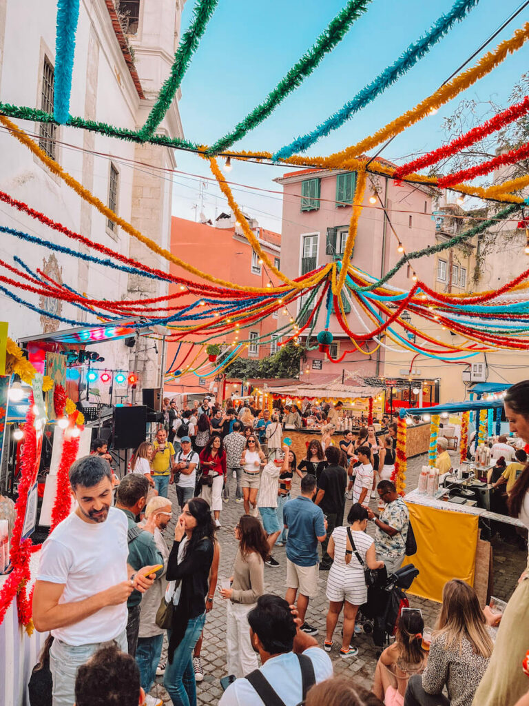 Crowds enjoying a lively street festival with colourful streamers overhead in a Lisbon neighbourhood – a festive experience to include during a weekend in Lisbon.