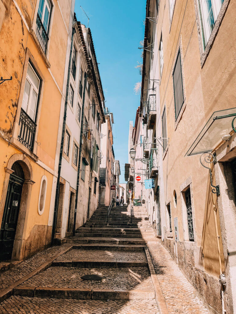 A quiet, narrow staircase street flanked by old buildings with pastel facades in the Alfama neighbourhood of Lisbon – a typical historic alleyway to explore during a 2-day Lisbon itinerary.