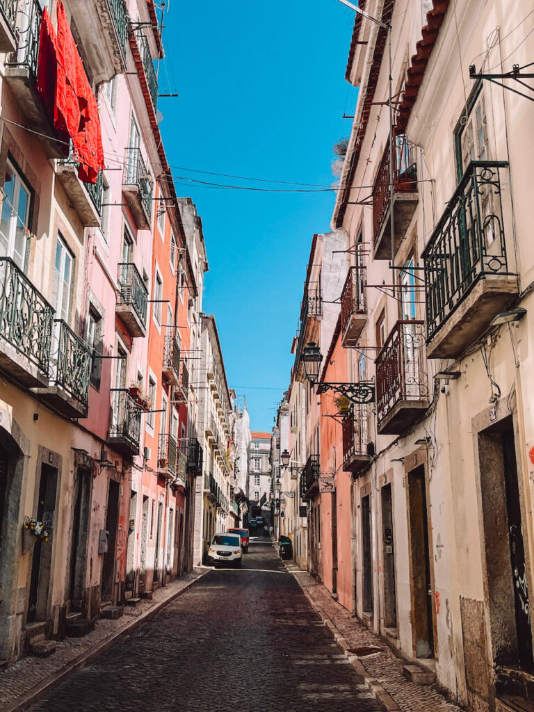 A cobblestone street in the Alfama neighbourhood lined with traditional Lisbon buildings in pink and cream tones – perfect for strolling and discovering hidden corners during your 2 days in Lisbon.