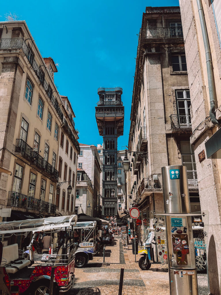 The Santa Justa Lift rising between historic buildings in Lisbon, with tuk-tuks and tourists at the base – a popular viewpoint and attraction for a 2-day Lisbon itinerary.