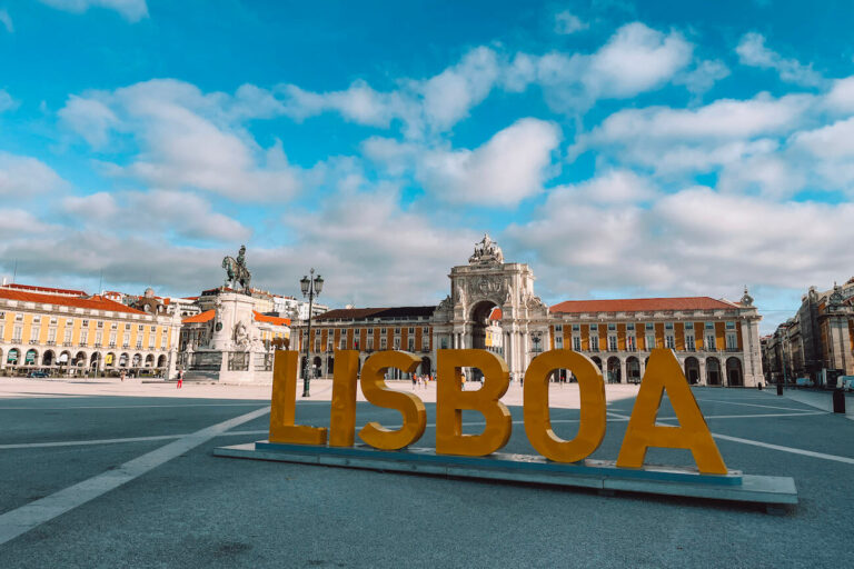 Large yellow "LISBOA" sign in front of the Praça do Comércio with the Arco da Rua Augusta and statue of King José I under a blue sky – a must-see landmark for a 2-day Lisbon itinerary.
