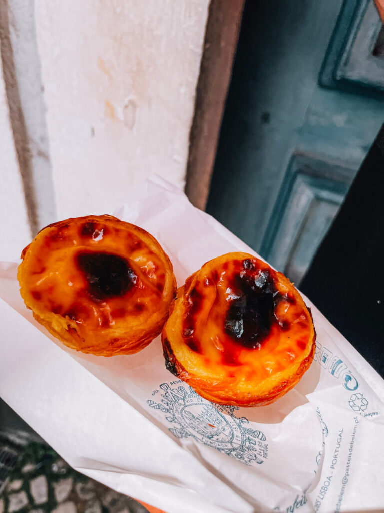 Two pastel de nata pastries on branded paper from Pastéis de Belém – an iconic Portuguese treat not to miss on any Lisbon itinerary.