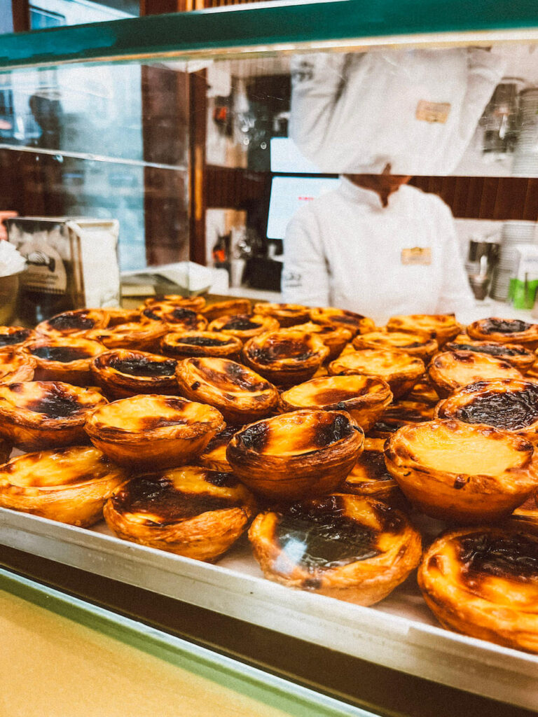 Glass display filled with freshly baked pastel de nata at a Lisbon bakery – sampling these is essential during any weekend in Lisbon.