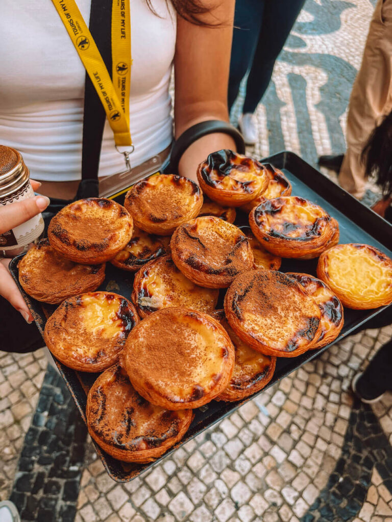 Tray full of pastel de nata being held by a tour guide on the streets of Lisbon – a delicious highlight on a culinary-focused 2-day Lisbon itinerary.