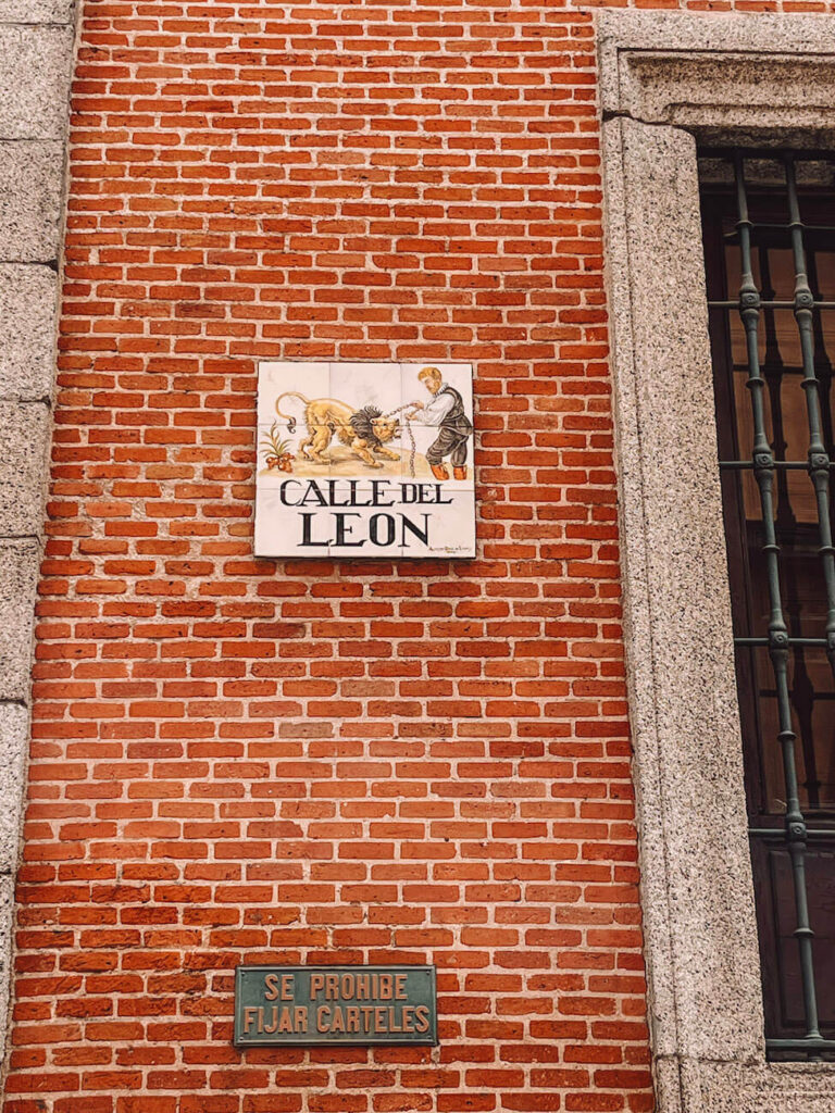 Decorative ceramic street sign for Calle del León against a red brick wall – a detail you may notice when wandering historic streets on your Madrid itinerary.
