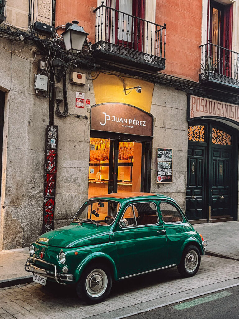 Vintage green Fiat 500 parked outside a traditional jamón shop in central Madrid – a charming street scene you might encounter during a first-time visit to Madrid.