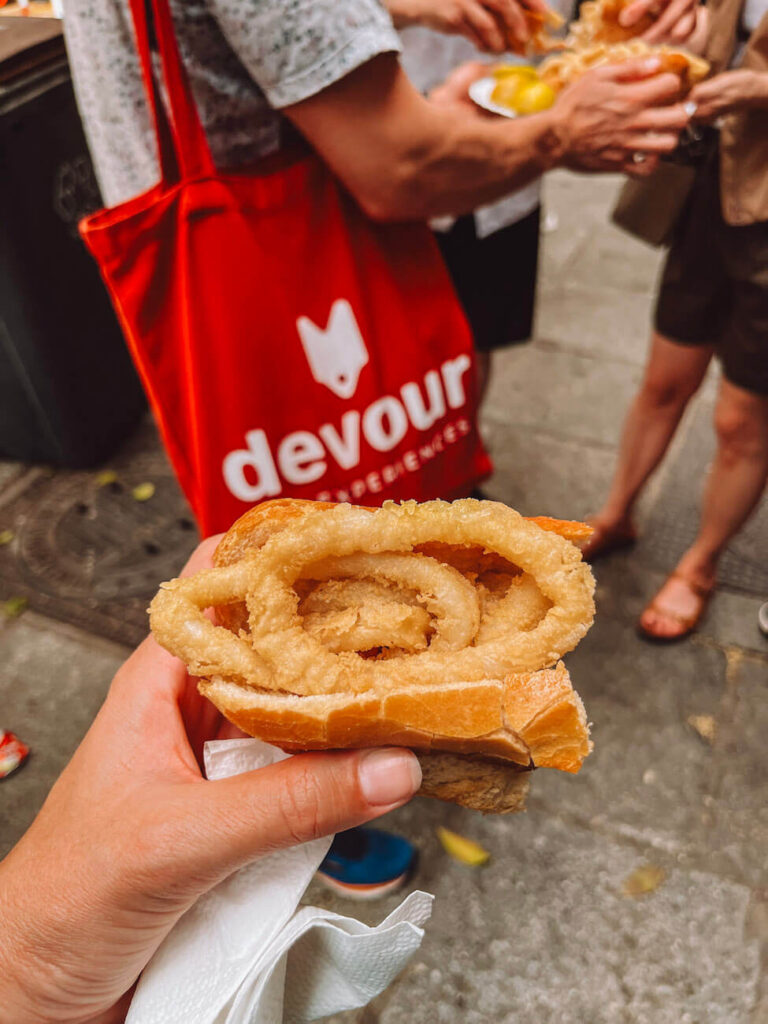 Traditional bocadillo de calamares (fried squid sandwich) being held at a street food stop – an essential dish to try during a weekend in Madrid. A Madrid food tour with Devour Tours is a must!