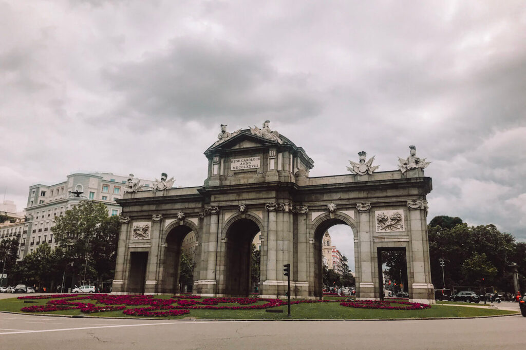 Puerta de Alcalá, a monumental neoclassical gate framed by flower beds and city traffic – one of Madrid’s most recognisable landmarks to visit in 2 days.