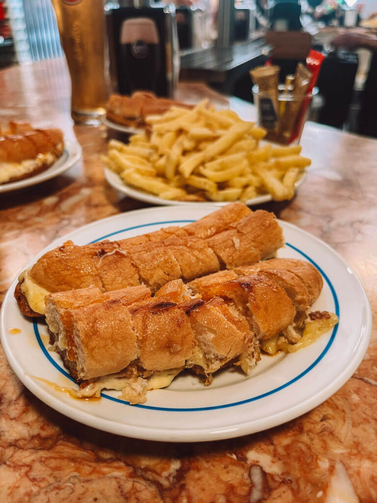 Close-up of a traditional Porto cachorrinho sausage sandwich served with fries and beer on a bar counter – a must-try dish during your 2 days in Porto.