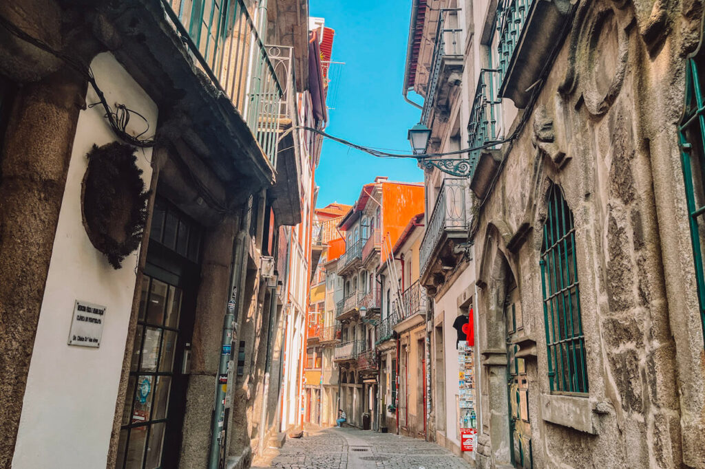 Narrow cobblestone alley in Porto’s historic centre, lined with old buildings, iron balconies, and laundry hanging above – a charming area to explore in Porto.