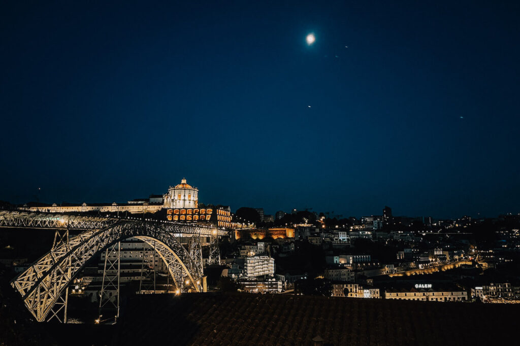 Night view of the illuminated Dom Luís I Bridge and Serra do Pilar Monastery under a full moon – a magical scene to experience during a Porto weekend.