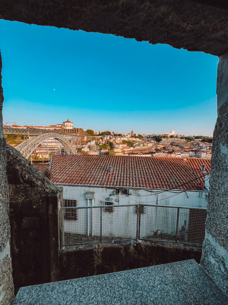Framed view of Porto’s rooftops and the Dom Luís I Bridge through a stone window opening – a hidden vantage point to discover in Porto.