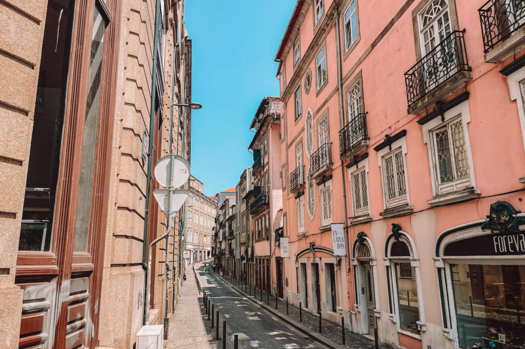 Quiet street in central Porto lined with pastel-coloured buildings, boutique signs and cobbled sidewalks – a picturesque place for a walk on your Porto itinerary.